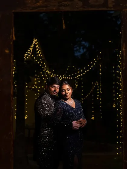 A romantic, moody portrait of a couple framed by a rustic doorway and twinkling fairy lights, perfect for a Sangeet or reception.