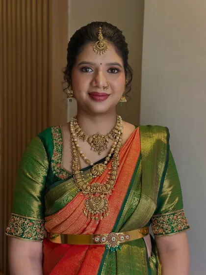 A frontal portrait of a beautiful South Indian bride. Her look features expertly blended eyeshadow and a rich lip color, complementing the intricate temple jewellery and embroidered blouse.