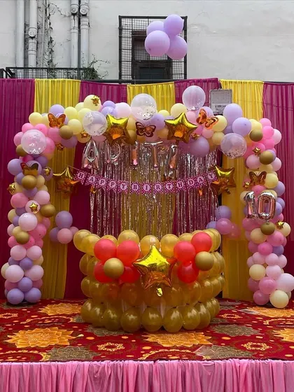 An outdoor birthday decoration setup in a tent. I used a combination of pink, yellow, and gold balloons to create a festive stage with a shimmer curtain backdrop.