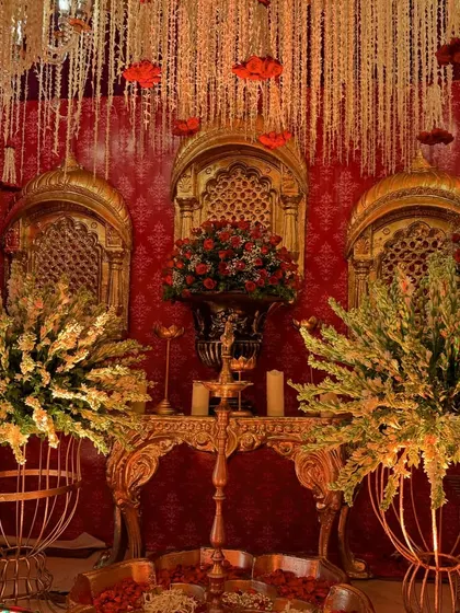 A detailed view of a side table arrangement, featuring golden jharokha-style windows, large floral bouquets in ornate vases, and a ceiling of hanging flowers.