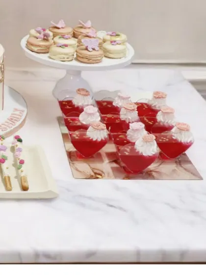 Another view of the ballerina dessert table, highlighting the variety of treats offered. You can see the butterfly-topped macarons, heart-shaped jelly cups, and floral chocolate sticks, all designed to complement the main cake and theme.