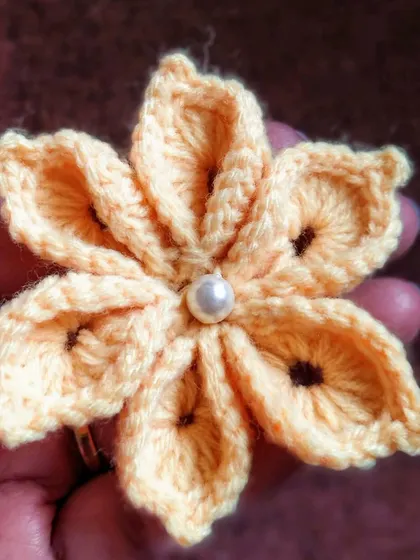 A delicate six-petal flower with a pearl center, held in my hand to show its size. I love experimenting with new floral designs for you.