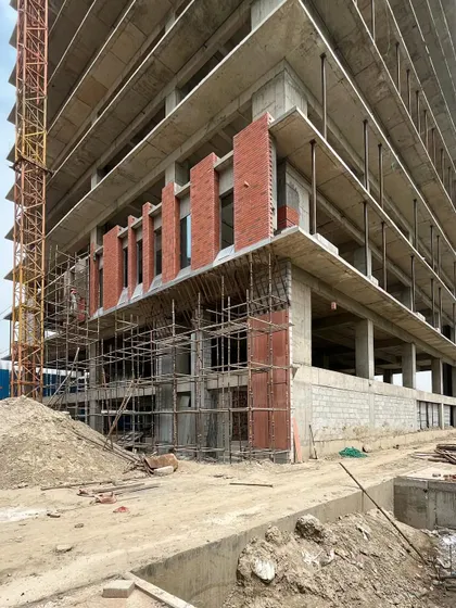 The brick facade work beginning on the lower floors of a commercial tower. This image captures the raw state of the construction site, with concrete and brick coming together.