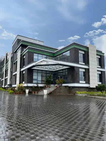 The entrance of Venkateshwar World School in Pune after a rain shower. The wet cobblestones reflect the building's facade, highlighting the material palette of grey stone, white GRC jalis, and green accents.