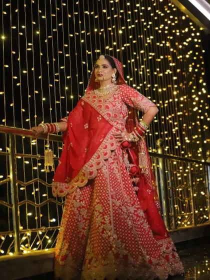 A full-length shot of a bride in a gorgeous red lehenga, posing against a backdrop of fairy lights. This showcases the entire look, including the outfit, makeup, and styling.