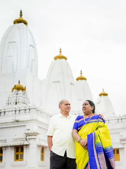 A stately portrait of a couple celebrating their 50th anniversary, standing before a beautiful white temple, symbolizing their long and blessed journey.