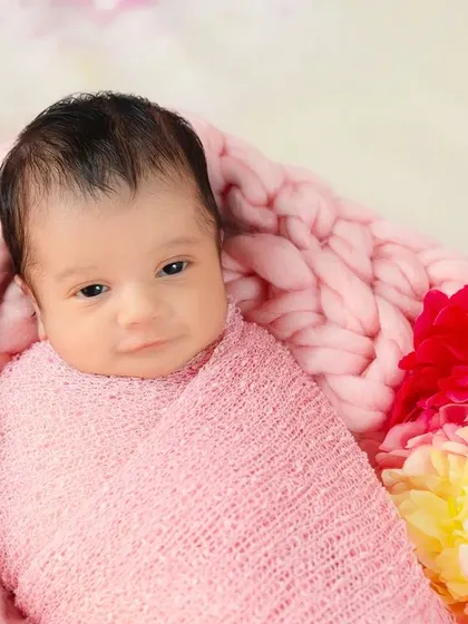 An adorable newborn, just starting to wake up, looks at the camera from a cozy, flower-filled basket. Capturing both sleeping and awake moments is part of the magic.