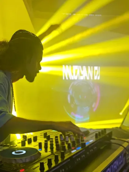 A profile shot of me at the decks, bathed in the yellow glow of the stage lights and my logo on the screen.