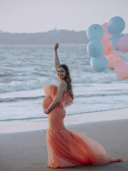A playful and happy beach photo featuring the peach mermaid gown. The addition of pink and blue balloons adds a celebratory touch, perfect for a gender reveal theme.