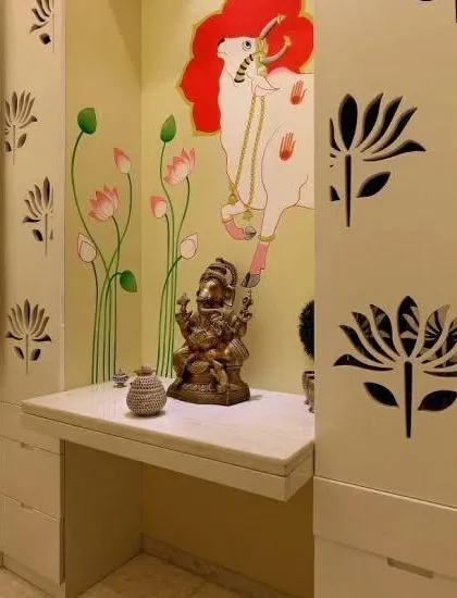 This custom pooja space combines modern cabinetry with traditional Indian art. The side panels of the unit feature delicate lotus jali cutouts, while the back wall is adorned with a hand-painted Pichwai-style mural of a cow and lotus flowers. It’s a wonderful way to create a unique and personal mandir within a niche in your home.