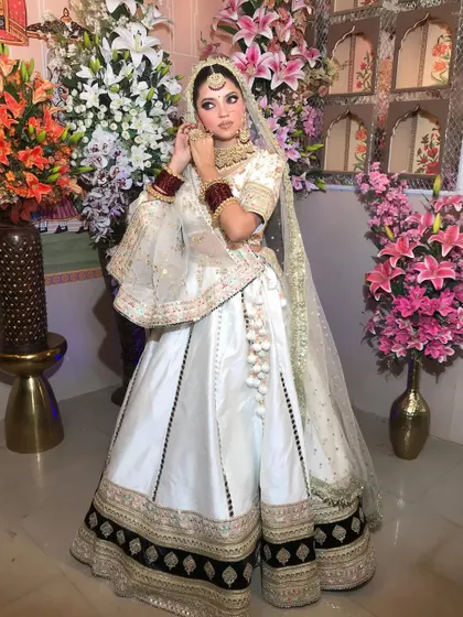 A stunning white Anarkali-style lehenga with a black and gold border. The flared sleeves and unique silhouette make it a standout choice for a modern bride.