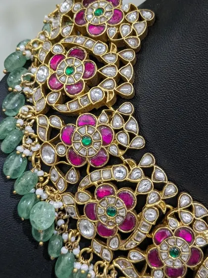 A close-up of a beautiful Jadau neckpiece, showing the vibrant pink and green stones and the quality of the uncut kundan.