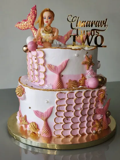 Another take on the mermaid theme, this two-tiered cake uses a pink and white palette. I created a mermaid scale texture with buttercream and added shimmering tails, shells, and a doll topper.