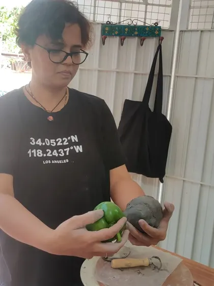 A student holds her sculpture next to the real capsicum, evaluating her work. This is a moment of reflection and learning in the creative process.