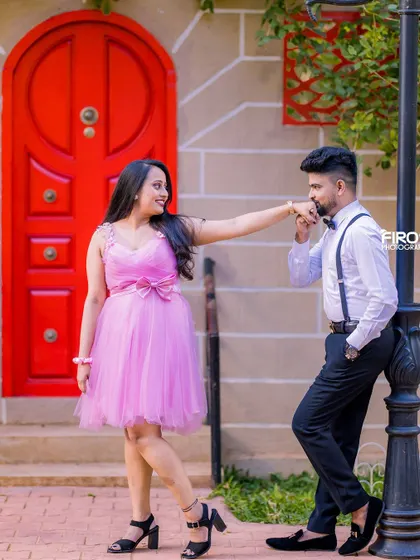 A classic romantic pose with a hand-kiss by a red door. The bride's pink dress and the groom's suspenders create a very sweet, vintage-inspired look.