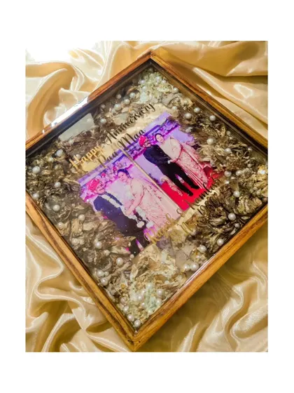 A beautiful shot of the anniversary keepsake, capturing the warm glow on the wooden frame and the sparkle of the gold leaf mixed in with the preserved flowers.