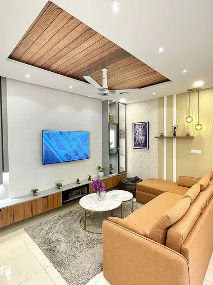 This living room is designed for comfort and style. A large L-shaped sofa in a warm mustard tone provides ample seating, while the wooden panel on the ceiling adds a touch of rustic charm.