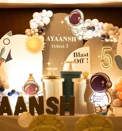 "Blast Off!" This space-themed setup for a fifth birthday features illuminated astronaut cutouts, a rocket, and marquee letters for a futuristic feel.