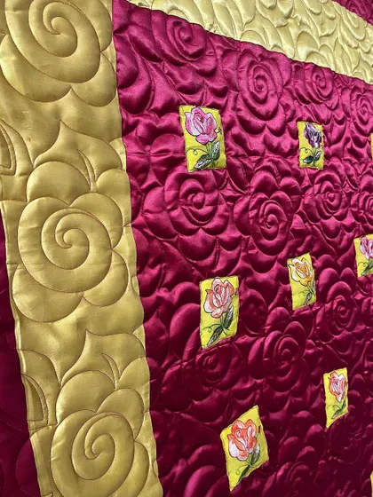 A close-up of a luxurious red and gold quilt, showing the large, swirling rose quilting pattern.