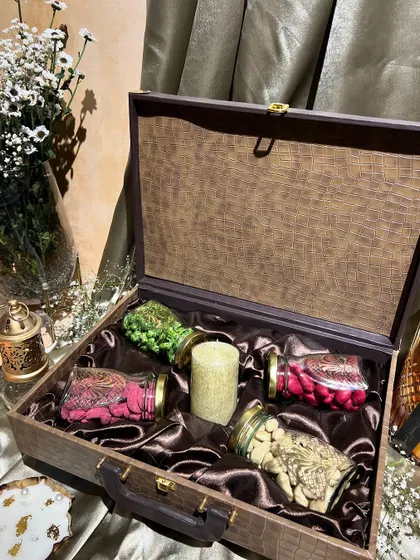 A rustic wooden trunk-style box for Diwali, lined with rich brown satin. It's filled with jars of dry fruits and a candle, perfect for a warm, earthy theme.