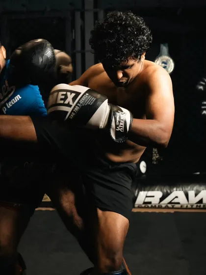 A fighter delivers a powerful knee strike to the coach's body during a clinch drill.