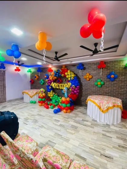 A wide view of the room decorated for a Cocomelon party. The setup includes a central balloon ring backdrop and smaller balloon clusters on the ceiling.