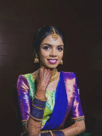 A close-up portrait showing the flawless skin and the beautiful contrast between the purple saree and the magenta lip color.