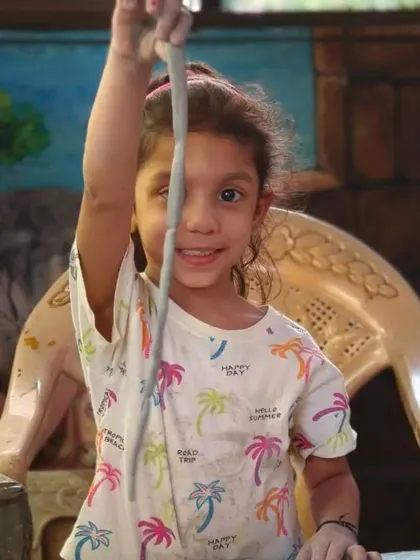 A young girl proudly holds up a long coil of clay, ready to use it for building her pot. Learning the coiling method is a key milestone for our budding potters.