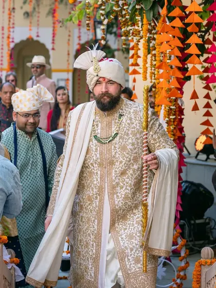 The groom makes his royal entrance with a staff, looking majestic in his white and gold sherwani.