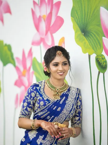 A duplicate of image 110, showing the bride in her royal blue saree against a floral backdrop.