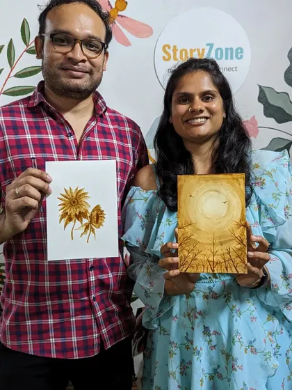 A couple proudly showing their coffee paintings. It's a unique medium that produces beautiful, sepia-toned artwork.