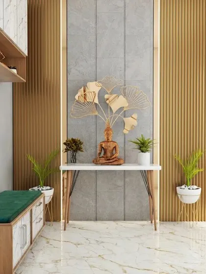 A modern and artistic entryway featuring a Buddha statue on a minimalist console table. The backdrop combines grey tile and gold-toned wood panels, with a large metal leaf sculpture adding a dramatic flair.