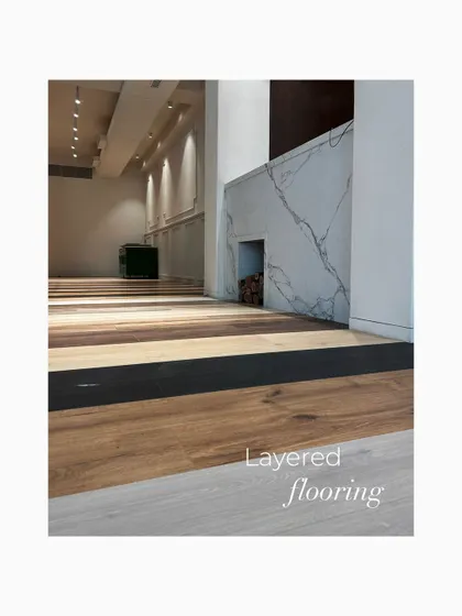 An early shot showcasing the layered flooring concept and the marble-clad fireplace structure. This image reveals the core material palette that defines the showroom's warm and tactile atmosphere.