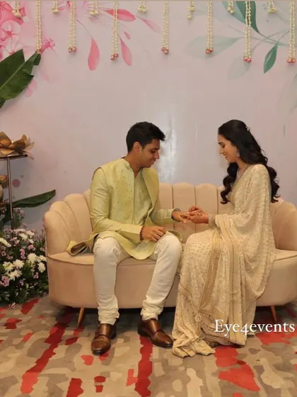 A happy couple sharing a moment during their ring ceremony. They are seated in front of our custom-designed pastel backdrop, which features delicate floral illustrations and hanging flower strings.