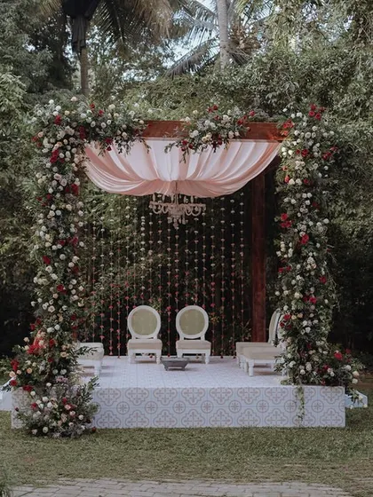 An elegant and romantic mandap for an outdoor wedding, featuring a cascade of flowers and a soft pink canopy set against a lush green backdrop at the Taj West End.