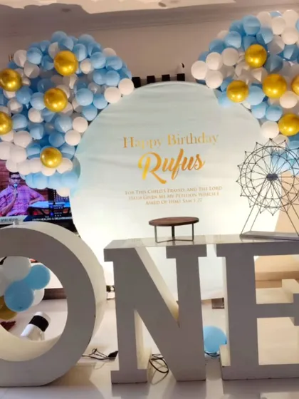 Large "ONE" letters are a popular and impactful prop for first birthday parties. This setup pairs them with a custom-printed backdrop and a blue and gold balloon arrangement.