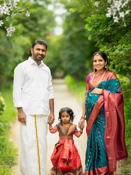 A perfect family portrait, with the parents and their young daughter holding hands and walking together in a beautiful park.