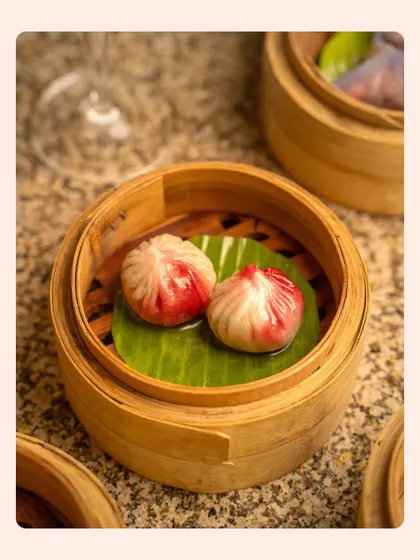 A detailed close-up of steamed dim sum in a traditional bamboo basket. The focus is on the delicate folds and colors of the dumplings, conveying authenticity and craftsmanship.