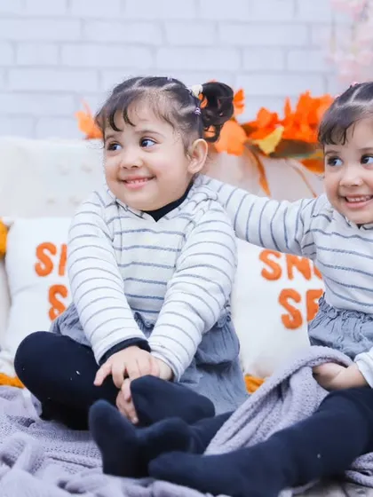 The twin sisters in a different outfit, smiling together in our cozy, autumn-themed "Snuggle Season" studio setup.