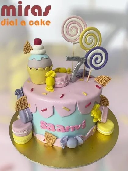 A candyland dream come true! This cake is overflowing with sweet treats, including lollipops, macarons, candies, and waffles, making it a paradise for anyone with a sweet tooth.