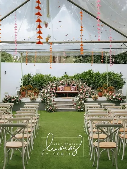 An ethnic-inspired baby shower setup under a clear tent. The stage is adorned with beautiful floral arrangements, creating a bright and celebratory space for the parents-to-be.