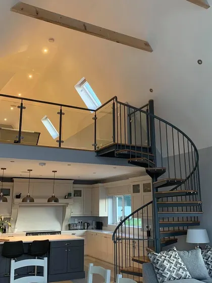 A bespoke spiral staircase connecting a living area to a mezzanine. It serves as a functional sculpture and a central feature of this beautiful open-plan home.