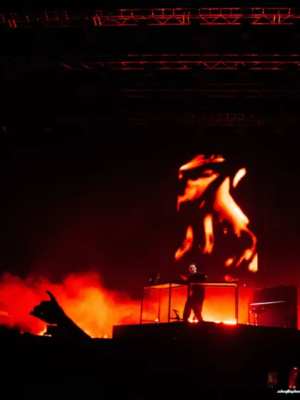 A wide, atmospheric shot of Ben Böhmer on stage, silhouetted against a fiery visual display. The image captures the scale of his solo performance.