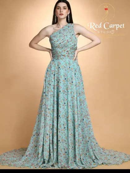A mannequin showcasing a one-shoulder gown in a light seafoam green floral print. The flowing fabric and long train make it a dreamy and ethereal choice for a summer event.