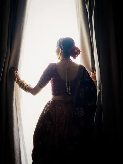 A silhouette of the bride, Khushi, as she looks out the window, a moment of quiet contemplation before her wedding.
