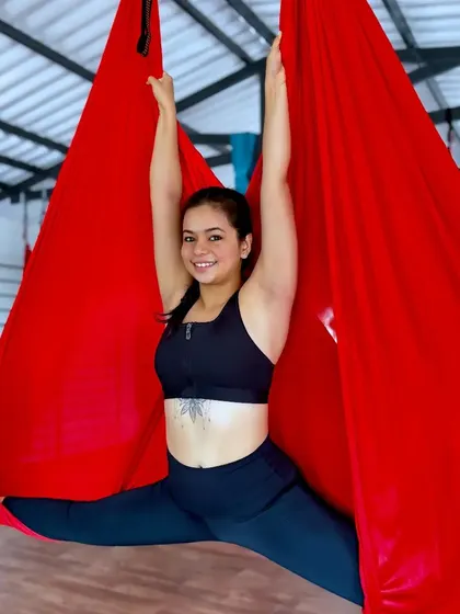 A student smiles while performing a split in the red aerial silk, a testament to the flexibility and strength gained through practice.