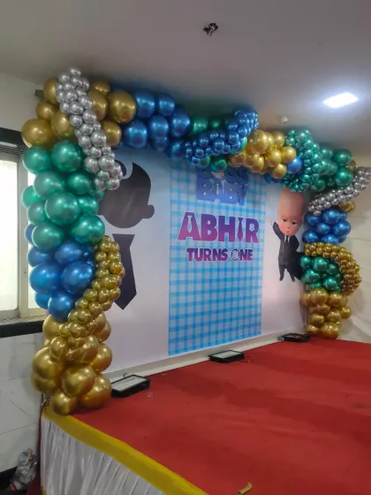 A balloon arch in blue, gold, and silver for a Baby Boss theme party, set up on a stage.