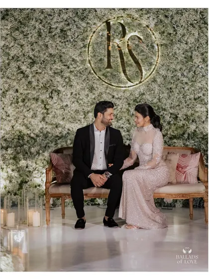 A happy couple posing in front of an elegant all-white floral wall at their reception. The custom monogram adds a personal touch to the sophisticated and modern decor.