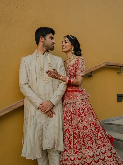 A regal portrait of the couple in their stunning red and cream wedding attire. We use architectural elements like staircases to add a touch of grandeur to our compositions.