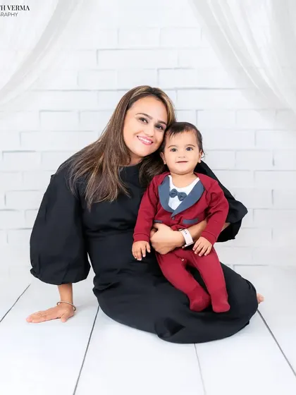 A mother sits with her baby boy, who is dressed in a cute tuxedo-style onesie. A sweet and stylish portrait against a clean white backdrop.